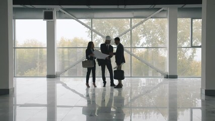 Wall Mural - Businesspeople are discussing real estate deal standing inside new modern building and studying construction plan against large panoramic windows