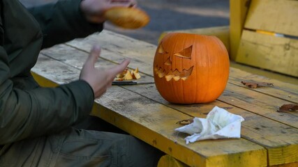 Wall Mural - Caucasian man finished carving the pumpkin and wipes his hands on a rag. Carved Jack O'Lantern pumpkin lies on yellow wooden table. Holiday handmade decorations theme. 4K resolution.