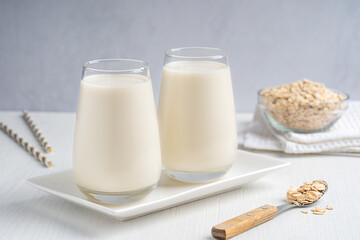 Wall Mural - Vegetarian lactose free oat milk made from whole grains with creamy texture and oatmeal-like flavor served in drinking glass on white wooden table with flakes, spoon and paper straws for breakfast