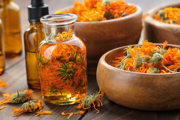 Bottles of calendula essential oil or infusion, wooden bowls and mortar of dried healthy calendula marigold flowers. Alternative herbal medicine. Aromatherapy.