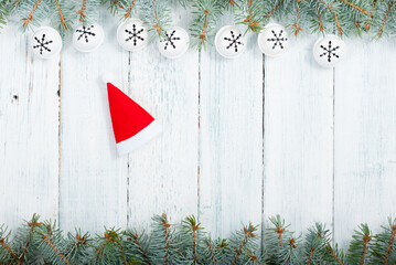 Wall Mural - Santa hat and pine tree branches frame with snowflake shape decorations on old wood table, Christmas background