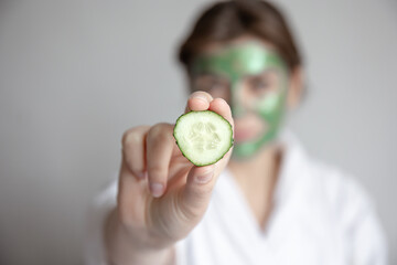 Wall Mural - Fresh cucumber slice in female hands on blurred background, spa concept.