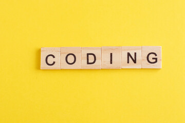 word coding made from wooden letters on yellow background. concept of learning programming languages