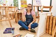 © Krakenimages.com - Young brunette woman at art studio sitting on the floor showing and pointing up with fingers number five while smiling confident and happy.