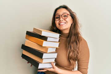 Wall Mural - Young hispanic girl holding a pile of books smiling with a happy and cool smile on face. showing teeth.