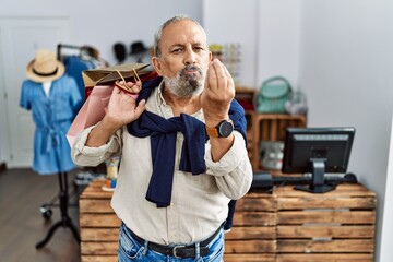 Poster - Handsome senior man holding shopping bags at boutique shop doing italian gesture with hand and fingers confident expression