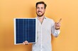 Handsome caucasian man with beard holding photovoltaic solar panel smiling happy pointing with hand and finger to the side