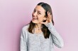 © Krakenimages.com - Young brunette woman wearing casual sweater smiling with hand over ear listening and hearing to rumor or gossip. deafness concept.