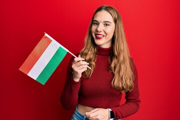 Poster - Young blonde woman holding hungary flag looking positive and happy standing and smiling with a confident smile showing teeth