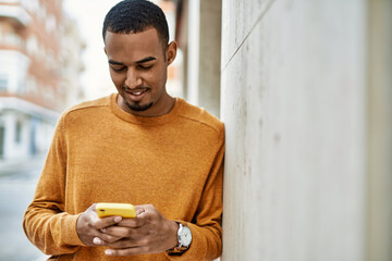 Wall Mural - Young african american man smiling happy using smartphone at the city.