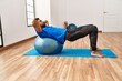 © Krakenimages.com - Handsome hispanic man doing exercise and stretching on yoga mat, practicing flexibility with pilates ball at the gym