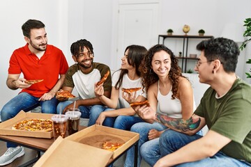 Wall Mural - Group of young friends smiling happy eating italian pizza sitting on the sofa at home.