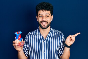 Sticker - Young arab man with beard holding heart organ smiling happy pointing with hand and finger to the side