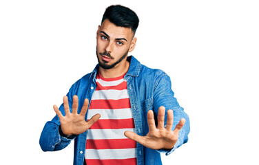 Young hispanic man with beard wearing casual denim jacket moving away hands palms showing refusal and denial with afraid and disgusting expression. stop and forbidden.