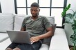 © Krakenimages.com - Young african american man using laptop at home sitting on the sofa skeptic and nervous, frowning upset because of problem. negative person.