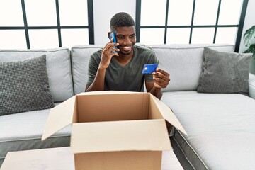 Sticker - Young african american man talking on the smartphone holding credit card at home