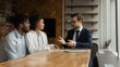 © fizkes - Positive smart young male real estate agent insurer lawyer giving professional consultation to happy family couple clients, making good propose or discussing good deal in modern office.