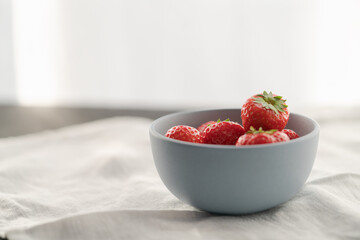 Wall Mural - Organic ripe strawberries in blue ceramic bowl on white linen cloth