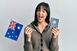 © Krakenimages.com - Young hispanic woman holding australian flag and passport winking looking at the camera with sexy expression, cheerful and happy face.