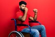 Arab man with beard sitting on wheelchair smelling something stinky and disgusting, intolerable smell, holding breath with fingers on nose. bad smell