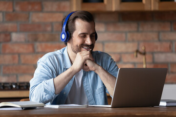 Wall Mural - smart remote student. smiling millennial man in modern earphones sit at domestic workplace by laptop