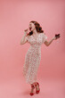 © Look! - Full length of glamorous young woman with small bowl in her hands eat cherry on pink background. Red-haired lady in summer time is dressed in long white dress and high heels.