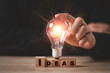 © Dilok - Businessman touching glowing light bulb on Idea wording print screen to wooden cube block for creative idea thinking and innovation concept.