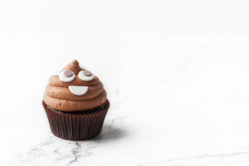 Wall Mural - Chocolate cupcake with brown cream cheese top decorated with mastic smiley face. Macro shot on the white background with copy space for text