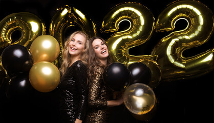 Happy gorgeous girls in stylish sexy party dresses holding gold 2022 balloons, having fun at Christmas or New Year's Eve Party.