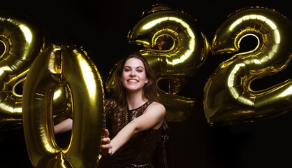 Wall Mural - Happy gorgeous girl in stylish sexy party dress holding gold 2022 balloons, having fun at Christmas or New Year's Eve Party.