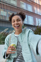 happy optimistic girl with two hair buns dressed in jacket enjoys free time and walking in city hold