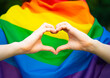 LGBT girl, lesbian woman shows sign in the shape of a heart with her fingers, hands on the background of the rainbow flag. Homosexual love, relationships.