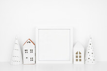 Christmas Mock Up With White Frame And White Tree And House Decor. Square Frame On A White Shelf Against A White Wall. Copy Space.