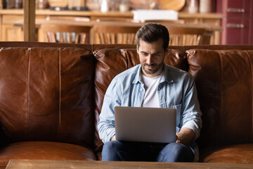 Wall Mural - working on pc. concentrated millennial male sit on comfortable couch at home use modern laptop hold 