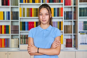 Wall Mural - Portrait of a confident teenage schoolgirl looking at the camera in the library.