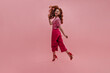 © Look! - Cheerful young woman bounces half sideways, smiling sweetly in studio shot. Model with red wavy hair flies to side, wearing T-shirt, crimson pants and red shoes. Elegant style, spring fashion trends.