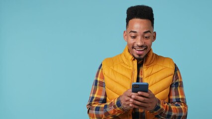 Wall Mural - Young african american†man 20s wears yellow shirt waistcoat hold use mobile cell phone point finger aside on workspace copy space mockup area isolated on pastel light blue background studio portrait