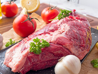 Wall Mural - A piece of fresh raw beef lies on parchment surrounded by spices, herbs and vegetables. Side view. Food composition