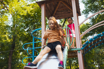 Wall Mural - The little girl is sitting on a slide in the playground