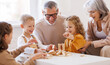 © JenkoAtaman - Excited children playing game Jenga at home with positive senior grandparents while sitting on sofa