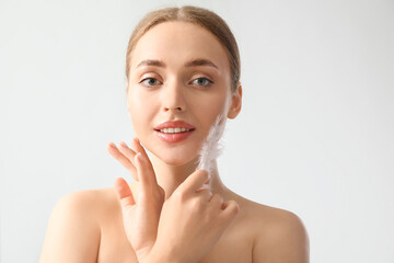 Wall Mural - Beautiful young woman with soft feather on light background