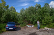 summer tourism and travel. white middle-aged man in a gray t-shirt and blue jeans resting on the river Bank. next to the white dog and blue car