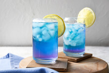 Glasses Of Iced Blue Tea And Lemon On Light Background, Closeup