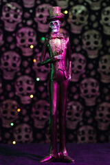 Sticker - Vertical shot of a Halloween figurine against a grungy skull wall with purple lights background