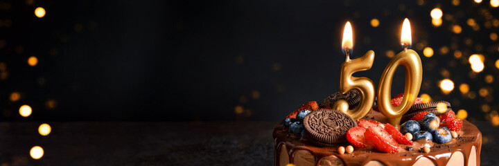 Banner with Chocolate birthday cake with berries, cookies and number fifty golden candles on black background, copy space