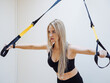 young beautiful fitness model with long blond hair in black activewear doing trx exercises