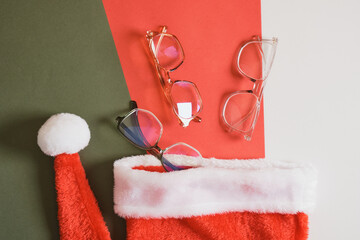 Wall Mural - eye glasses and santa hat on red and green background, optics store sale before christmas copy space