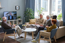 Group Of Senior People Resting On Sofa In The Living Room And Watching News On TV Together