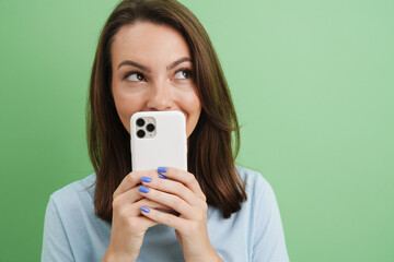 Wall Mural - Young brunette woman looking aside while posing with cellphone