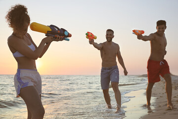 Wall Mural - Friends with water guns having fun on beach at sunset